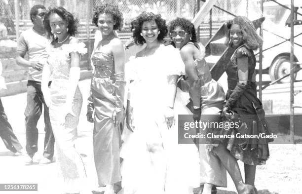 Photograph of a group of young women wearing formal dresses, they posed for the photograph by standing in a line and smiling, a man in a t-shirt and...