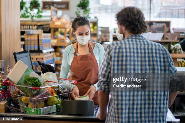 mann checkt an der kasse im supermarkt und menschen tragen gesichtsmasken - convenience store counter stock-fotos und bilder