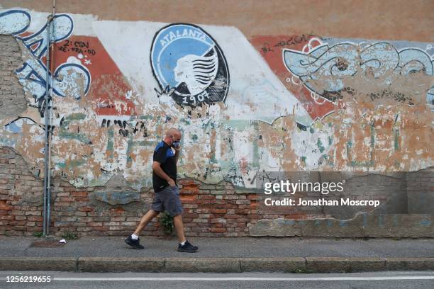 Man wearing a protective face mask walks past a club crest painted on a building facade outside the ground before the Serie A match between Atalanta...