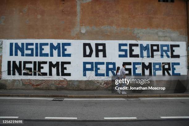 Couple wearing protective face masks walk past a slogan painted on a building facade outside the ground before the Serie A match between Atalanta BC...