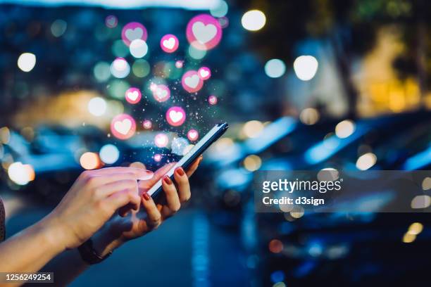cropped hand of young asian woman using smartphone on social media network application on the go, viewing or giving love in the city at night. social media addiction concept - facebook like stock pictures, royalty-free photos & images