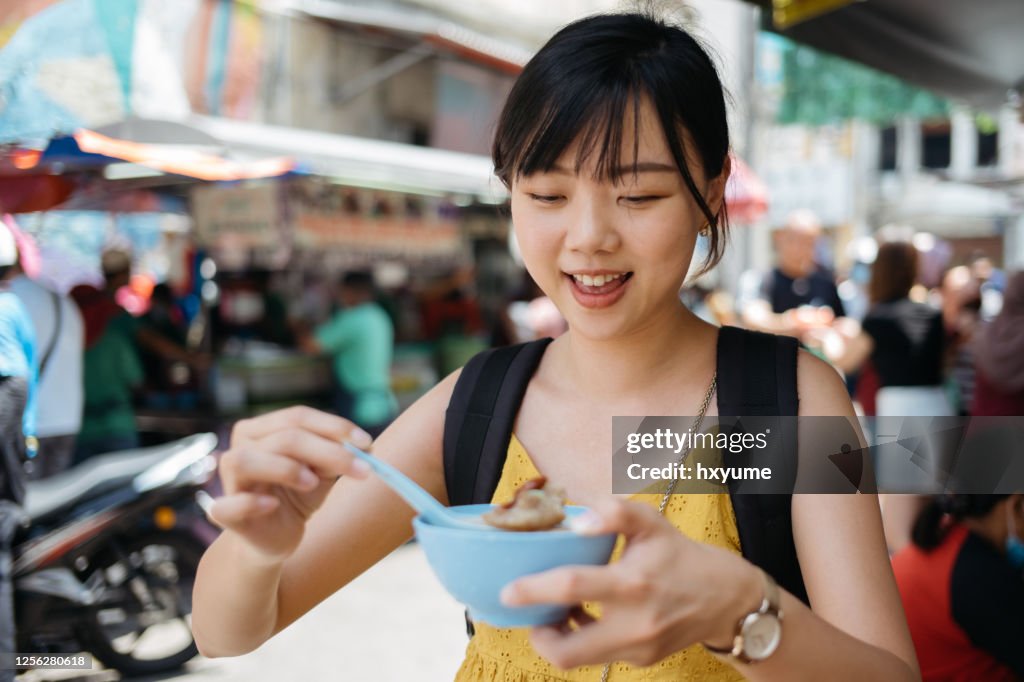 Young asian female tourist enjoying shaved ice dessert cendol at street