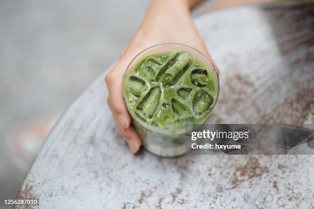 young female hand holding a glass of japanese ice matcha latte - latte stock pictures, royalty-free photos & images