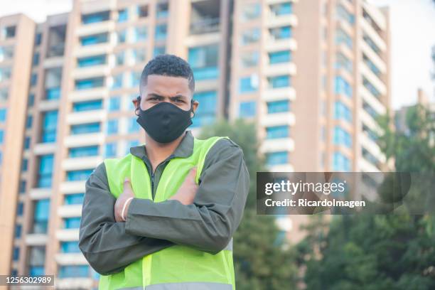 arbeiter schaut in einem porträt in die kamera, während er seine arbeitsuniform und anti-covid 19 maske vor seinem job trägt - anti quarantäne protest stock-fotos und bilder