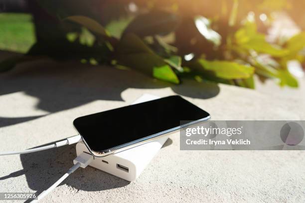 mobile smart phone charging wirelessly by sharing battery via device on a sunny day on a background of green leaves. - powerbank stock-fotos und bilder