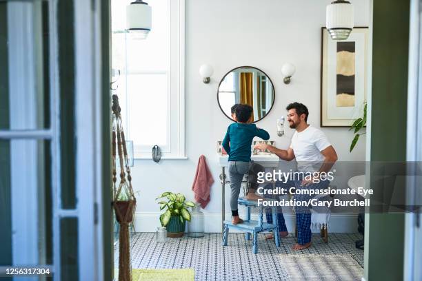 Father helping son brushing teeth in bathroom