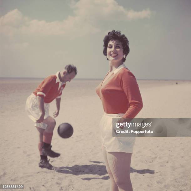 English singer Alma Cogan posed with English footballer and captain of Blackpool FC, Harry Johnston on a beach near Blackpool, England in August...