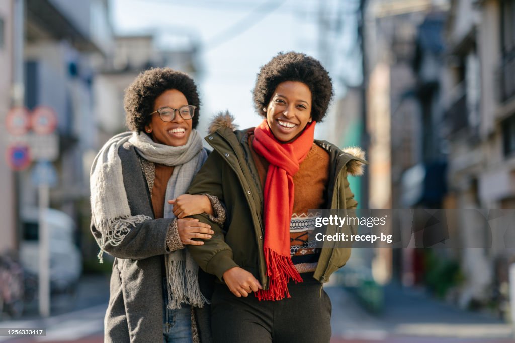 Hermanas gemelas negras caminando en la calle brazo en brazo felizmente