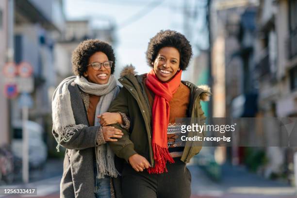 black twin sisters walking in street arm in arm happily - sibling stock pictures, royalty-free photos & images