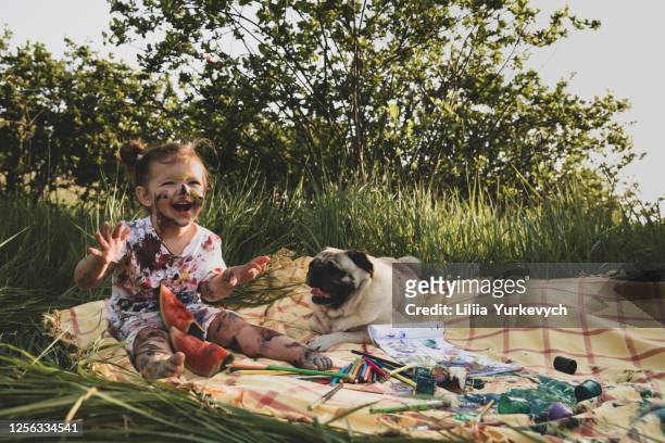 a little girl stained in paint is playing with her dog in the forest. - baby paint stock-fotos und bilder