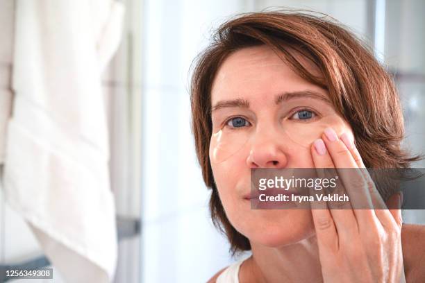 portrait of beautiful senior woman applying makeup on white background of bathroom. - trattamento di bellezza foto e immagini stock