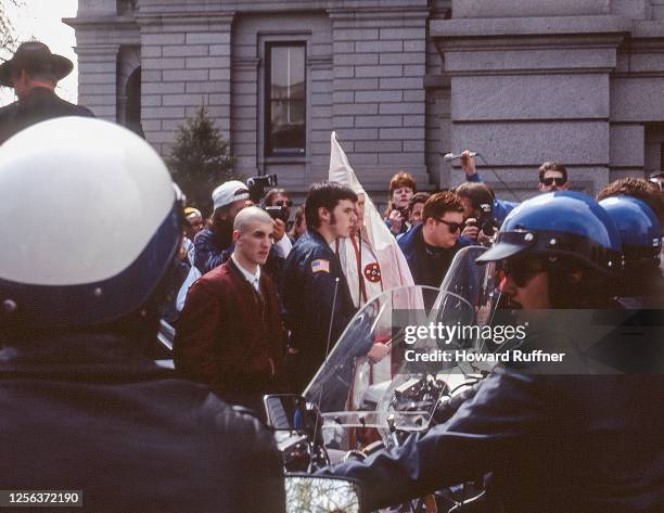 Surrounded by police and anti-Klan demonstrators, an unidentified KKK member escorted by several skinheads arrives at the Colorado State Capitol...