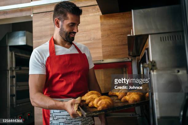 baker taking fresh pastry out of the oven - dedication stock pictures, royalty-free photos & images