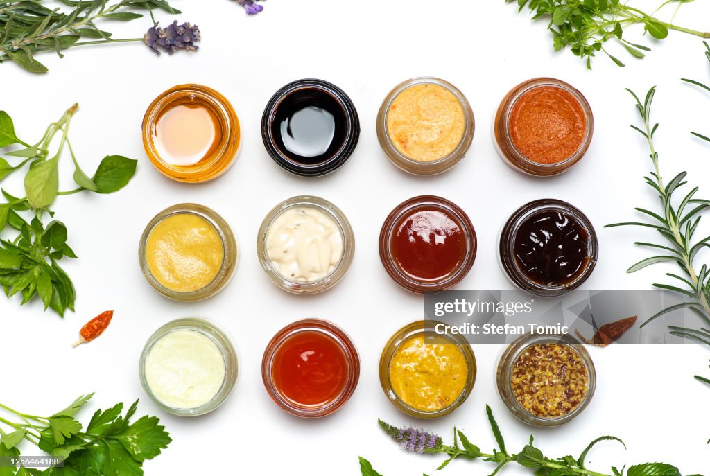 Grote inzameling van sauzen en gekruide uitspreidingen in kleine potten die plat worden geïsoleerd leggen