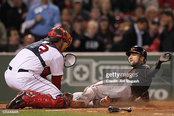 Nick Markakis of the Baltimore Orioles scores a run in the first inning as Jason Varitek of the Boston Red Sox defends in the second game of a...