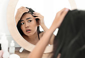 Worried asian woman checking her hair in mirror at home