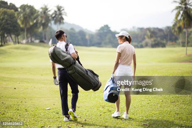asia chinese couple walking together in the golf course with their golf bags. - golf accessories stock pictures, royalty-free photos & images