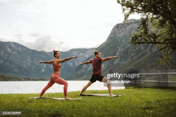 two persons doing yoga at the scenic lake - warrior 2 stock pictures, royalty-free photos & images