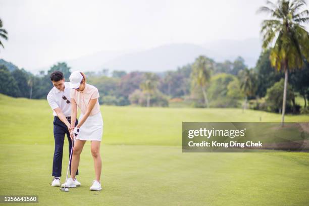 an chinese golf pro teaching his wife on putting green - golf lessons stock pictures, royalty-free photos & images