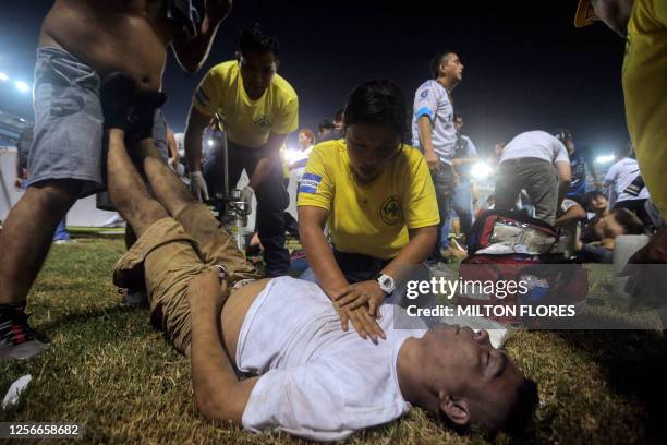 Rescuers attend an injured man lying on the pitch following a stampede during a football match between Alianza and FAS at Cuscatlan stadium in San...