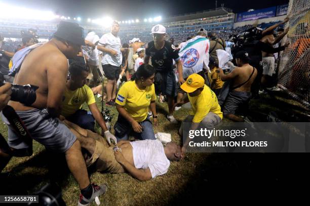 Rescuers attend an injured man lying on the pitch following a stampede during a football match between Alianza and FAS at Cuscatlan stadium in San...