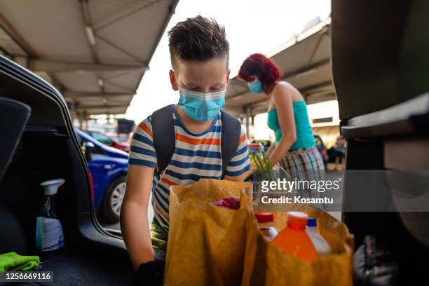 diligent 9 years old son helping his mother to pack groceries into car trunk after shopping - 8 9 years stock pictures, royalty-free photos & images