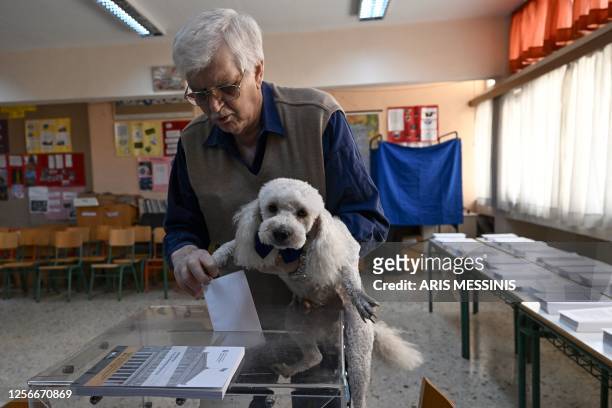 Voter carrying his dog casts his ballot at a polling station on the general elections day in Athens on May 21, 2023. Greece goes into the polls in...