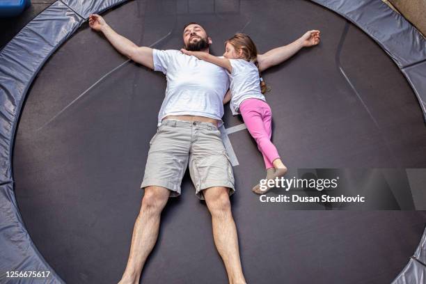 vater und seine kleine tochter liegen auf einem trampolin - trampoline stock-fotos und bilder