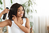 Hairstyling. Smiling Black Woman Applying Texturising Spray To Her Beautiful Curly Hair