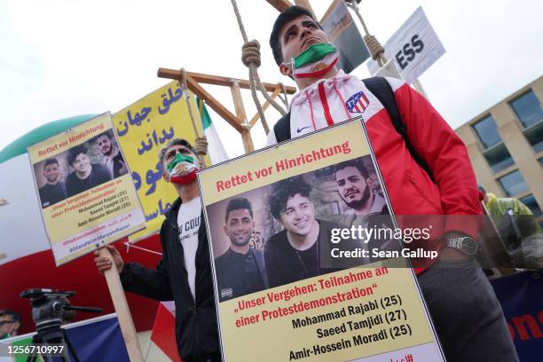 Demonstrators wearing hangman's nooses hold portraits of Amirhossein Moradi, Mohammad Rajabi and Saeed Tamjidi, who took part in street...