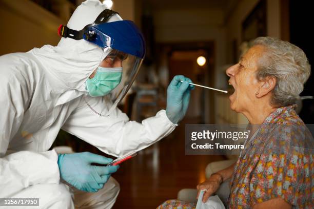 doing a covid test in full ppe wear at a senior's home. - infectious disease control stock pictures, royalty-free photos & images