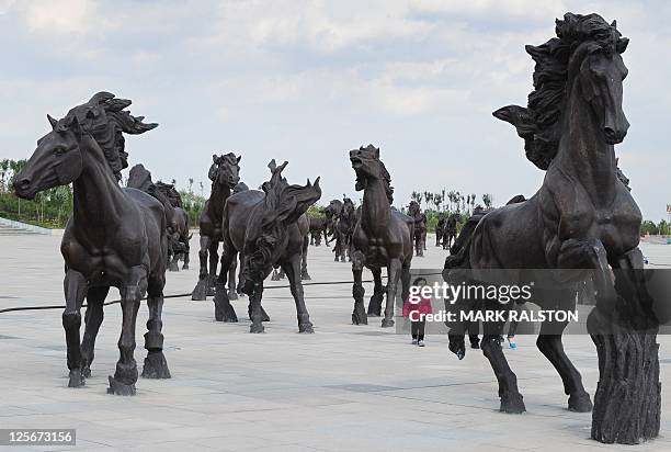 Young girl walks amongst horse statues built as a tribute to Genghis Khan whose unmarked tomb is claimed to be nearby, in the city of Ordos, Inner...