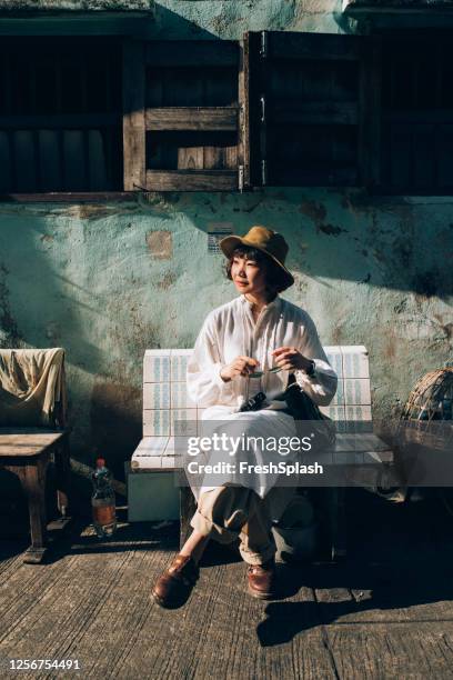 dans les rues de bangkok : une jeune femme asiatique assise sur un banc dans la vieille ville - daily life in bangkok photos et images de collection