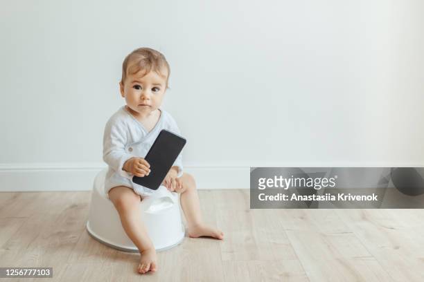 funny toddler sitting on white potty chair and playing mobile phone. - baby pee stockfoto's en -beelden