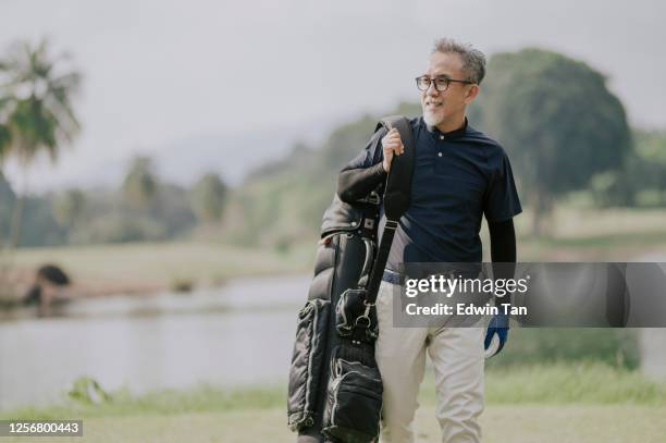 een gerijpte chinese man golfer die een golftas die weg in de golfcursus kijkt - men's water polo stockfoto's en -beelden