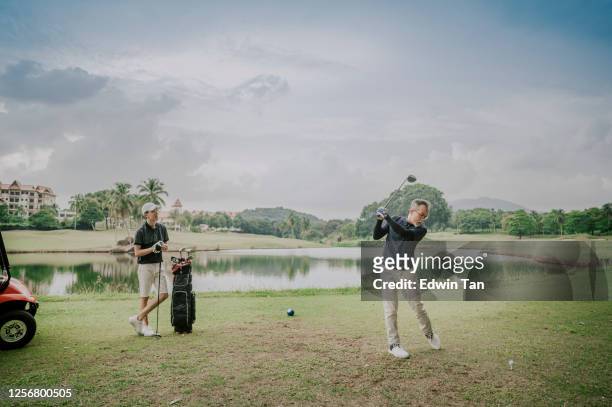 an asian chinese mature guy tee off swing his driver club at tee off point golf course in weekend while his son watching - play off stock pictures, royalty-free photos & images