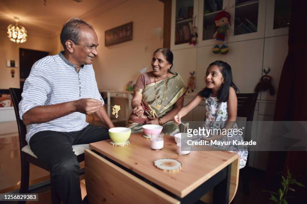 senior couple enjoying snacks with granddaughter - daily life in india stock pictures, royalty-free photos & images