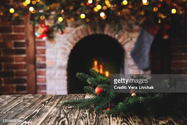 christmas tree branch on a wooden table against the background of a fireplace, place for text, christmas concept, christmas toys and blurry lights - weihnachtstisch stock-fotos und bilder