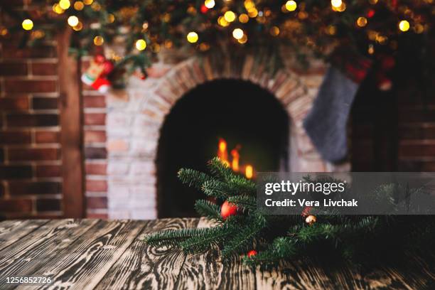 christmas tree branch on a wooden table against the background of a fireplace, place for text, christmas concept, christmas toys and blurry lights - cosy background stock pictures, royalty-free photos & images