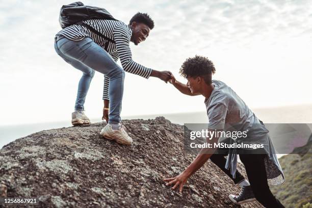 young man helping his friend to climb the rock - black top stock pictures, royalty-free photos & images