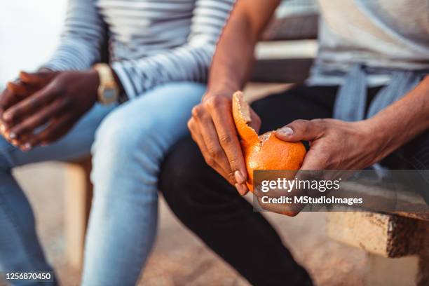 hombre pealing naranja mientras está sentado con un amigo en el banco - mondo fotografías e imágenes de stock