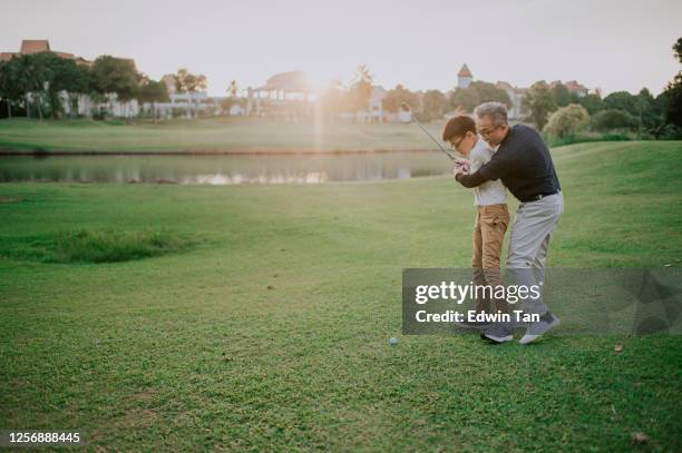 an asian chinese senior man golfer teaching his grandson how to play golf at golf course during sunset - bent golf club stock pictures, royalty-free photos & images