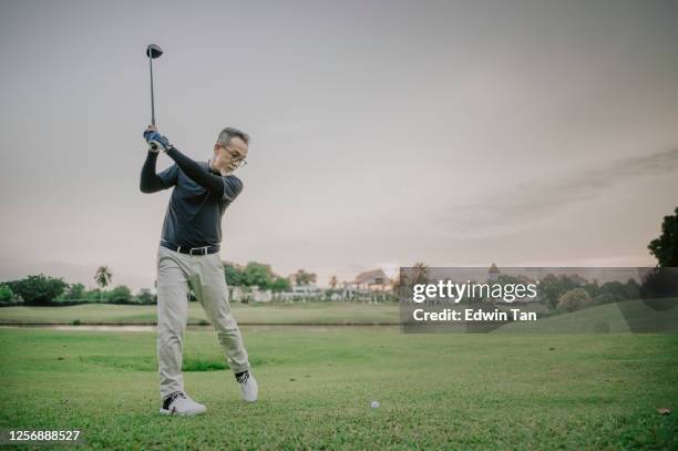 an asian chinese mature guy tee off swing his driver club at tee off point golf course in weekend - golf swing sunset stock pictures, royalty-free photos & images