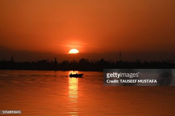 Men steer a boat during sunset in Dal Lake in Srinagar on May 21, 2023.