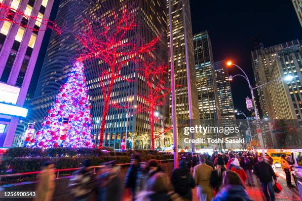 big christmas tree glows among the high-rise buildings in the night at midtown manhattan new york city. - rockefeller centre photos et images de collection