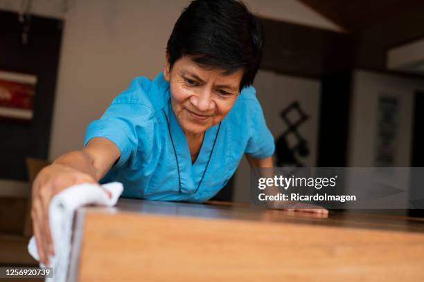 limpiando la mujer latina limpia la mesa de madera de la casa que trabaja para - mature latin women fotografías e imágenes de stock