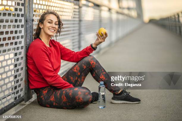 athletische frau ruht nach einem harten training, essen apfel und trinkwasser im freien - frau apfel stock-fotos und bilder