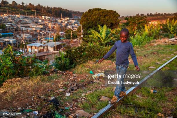 bambino africano che cammina sui binari della ferrovia, baraccopoli di kibera sullo sfondo, kenya, africa orientale - nairobi foto e immagini stock