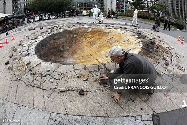 British artist specialized in pavement drawings, wall murals and realistic paintings, Julian Beever, works on his pavement painting of a crater at...