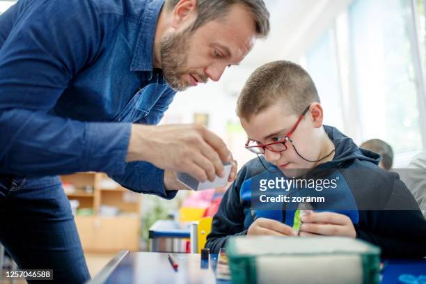 speciale behoeften jongen die leraar let die hem toont hoe om document te vouwen - special needs stockfoto's en -beelden